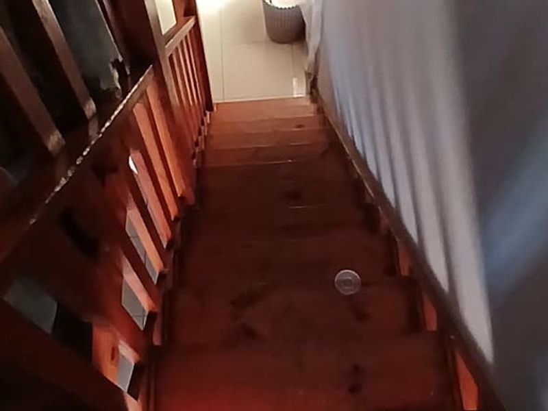 A steep timber staircase with a wooden balustrade leading to a lower level, showing signs of wear on the wooden treads.