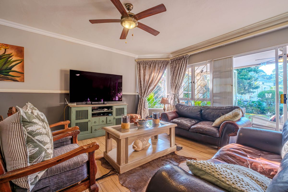 A comfortable living room featuring tiled flooring, a ceiling fan, and large sliding glass doors that provide access to the outdoor area.
