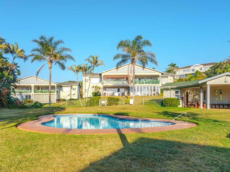 A well-maintained communal pool area set within a landscaped garden, featuring brick coping and views of the apartment complex buildings.