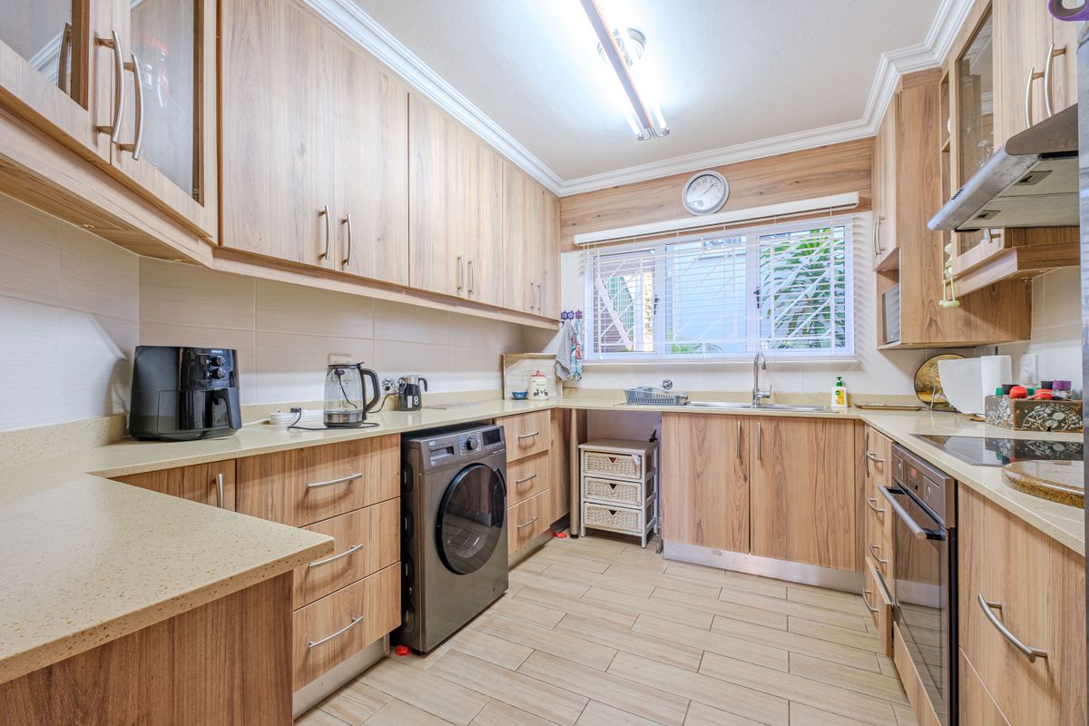 A functional kitchen featuring wood-look laminate cabinetry, stone countertops, built-in oven, extractor fan, and tiled flooring with ample storage space.