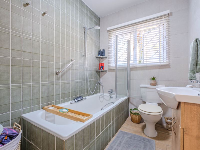 A well-maintained bathroom featuring a bathtub with a glass shower screen, tiled walls, a vanity basin, and a toilet.