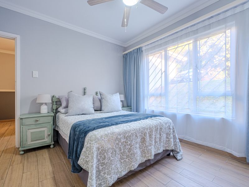 A well-maintained bedroom featuring tiled flooring, crown molding, a ceiling fan, and large windows fitted with security bars.