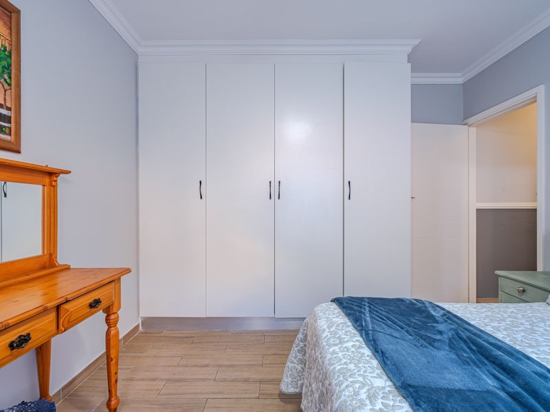 A well-maintained bedroom featuring neutral walls, tiled flooring, crown molding, and ample built-in cupboard storage.