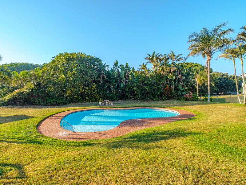 A well-maintained kidney-shaped swimming pool set within a spacious, landscaped garden area with mature trees and lawn.