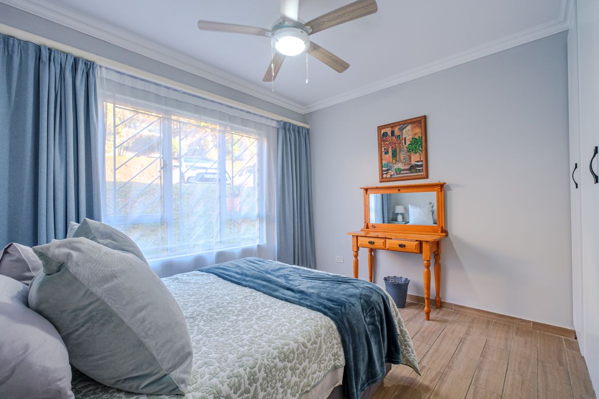 A well-maintained bedroom featuring tiled flooring, a ceiling fan, and built-in cupboards, with natural light provided by a window fitted with security bars.
