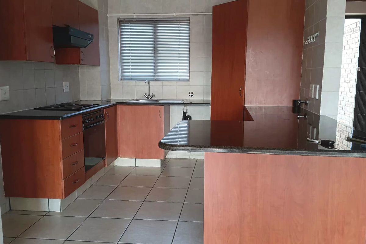 A functional kitchen featuring wood-finish cabinetry, granite countertops, built-in oven and hob, and tiled flooring with a breakfast bar area.