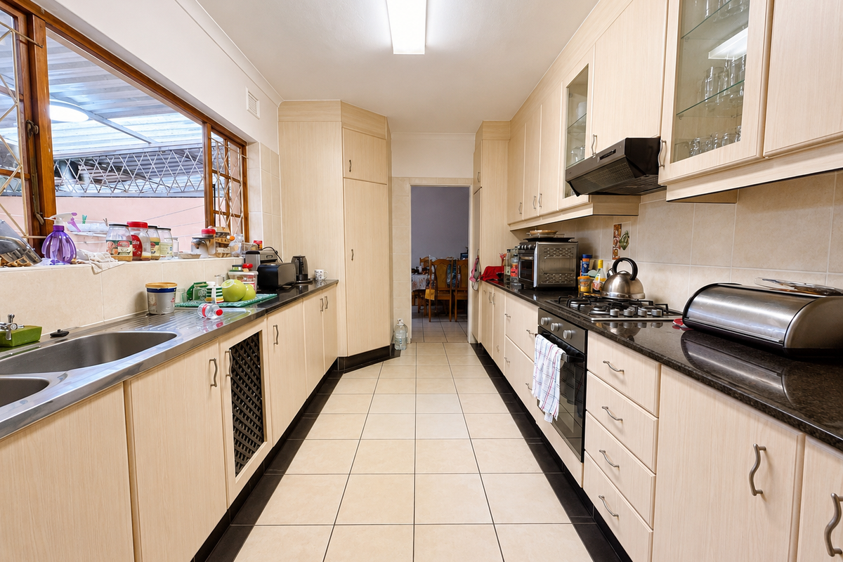 A functional galley-style kitchen featuring light wood cabinetry, granite countertops, a gas hob, and tiled flooring with ample storage space.