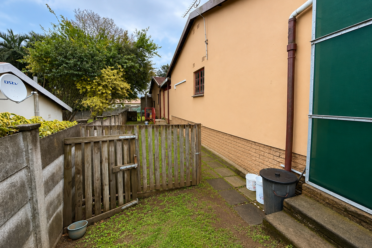 A view of the rear exterior area featuring a paved walkway, wooden fencing, and concrete boundary walls along the side of the house.