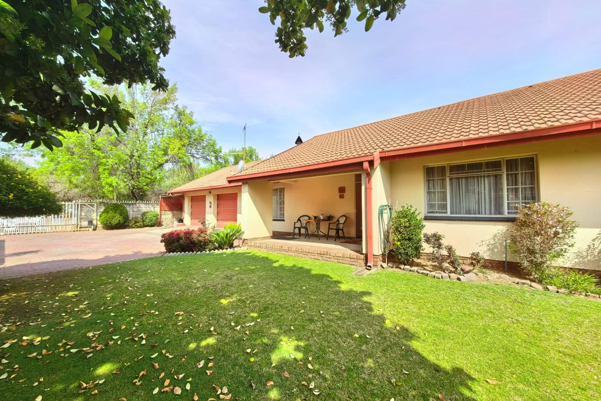 A well-maintained rear exterior view featuring a covered patio, a spacious lawn, and a double garage with a paved driveway.