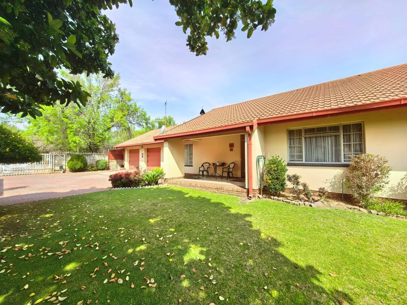 A well-maintained rear exterior view featuring a covered patio, a spacious lawn, and a double garage with a paved driveway.