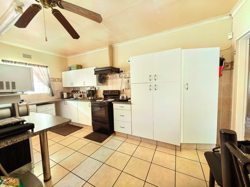 Functional kitchen featuring tiled flooring, built-in cabinetry, a freestanding stove with extractor fan, and ample storage space including a large pantry cupboard.