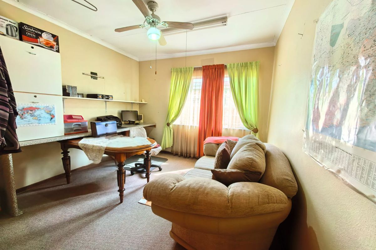 A functional bedroom or study space featuring a built-in desk, shelving, and a ceiling fan, offering potential for modernization and cosmetic updates.