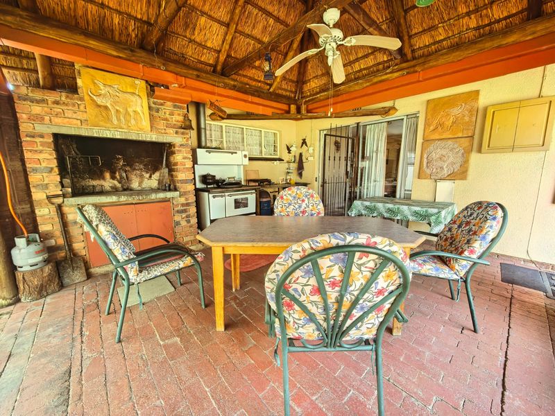 Covered outdoor patio featuring a traditional thatched roof, built-in brick fireplace, and brick flooring, providing a rustic space for outdoor entertaining.