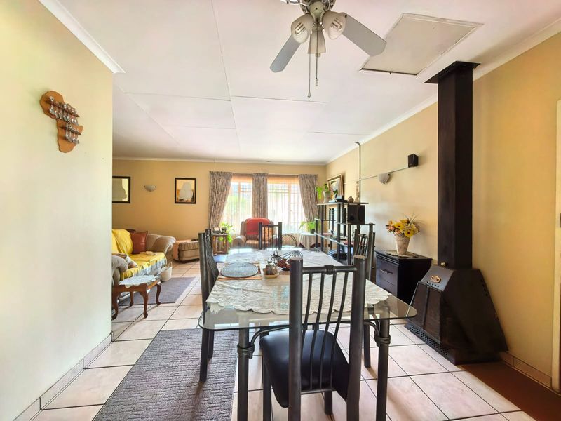 Open-plan living and dining area featuring tiled flooring, a ceiling fan, and a prominent freestanding fireplace.