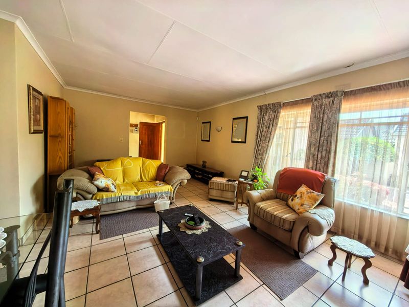 A spacious living room featuring tiled flooring, coved ceilings, and large windows that provide ample natural light.