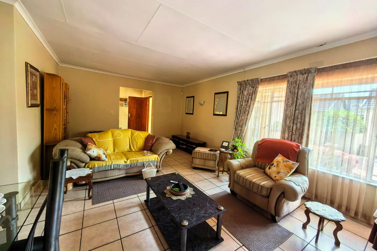 A spacious living room featuring tiled flooring, coved ceilings, and large windows that provide ample natural light.
