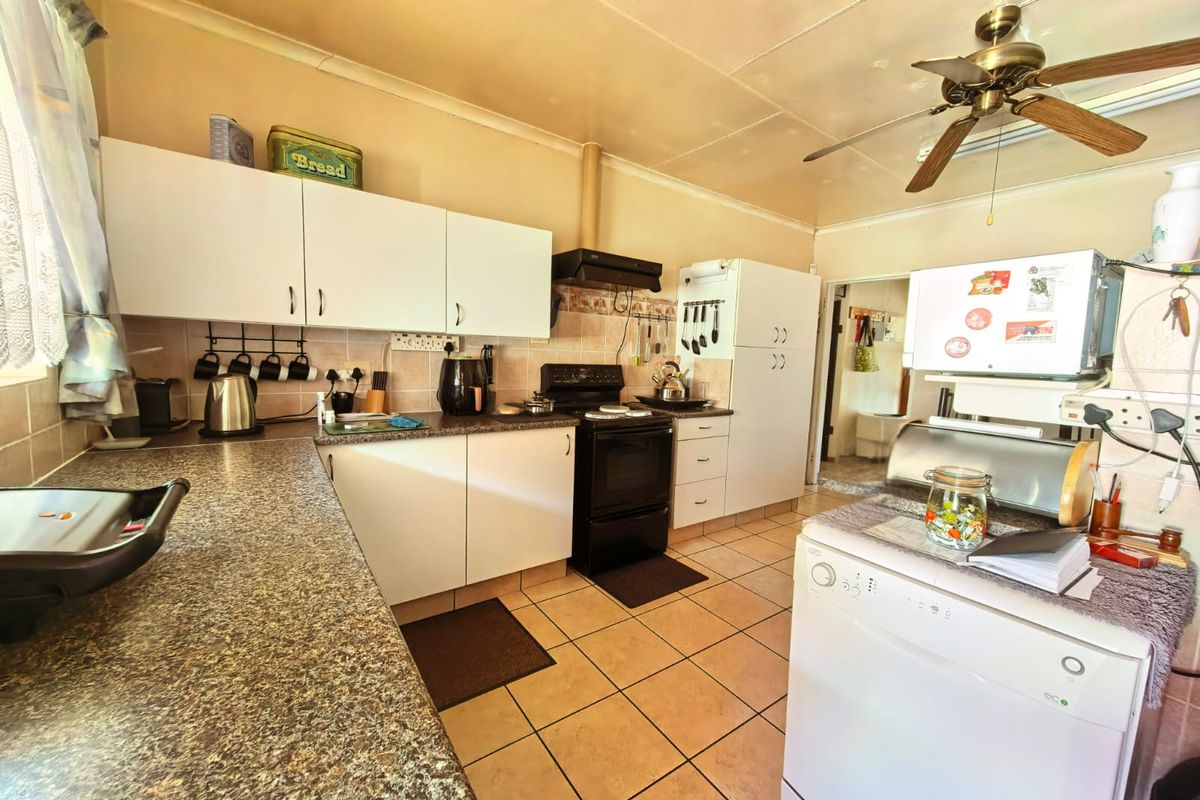 A functional kitchen featuring laminate countertops, white cabinetry, tiled flooring, and a ceiling fan, offering a practical layout with potential for modern updates.