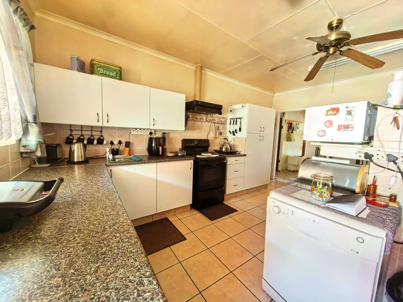 A functional kitchen featuring laminate countertops, white cabinetry, tiled flooring, and a ceiling fan, offering a practical layout with potential for modern updates.