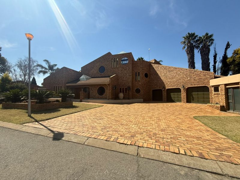 A distinctive face-brick residence featuring unique circular windows, multiple skylights, a spacious paved driveway, and an integrated double garage.