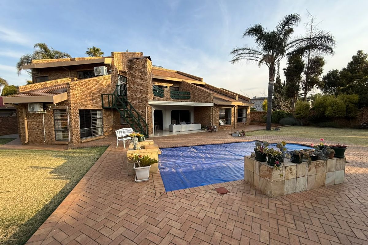 Rear view of a multi-level brick house featuring a paved patio area, a swimming pool with a cover, and an external metal staircase.