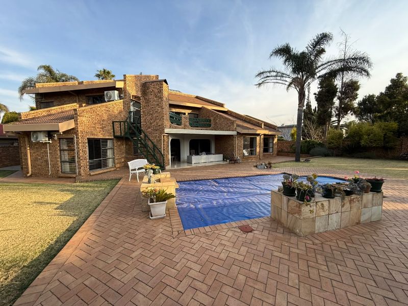 Rear view of a multi-level brick house featuring a paved patio area, a swimming pool with a cover, and an external metal staircase.