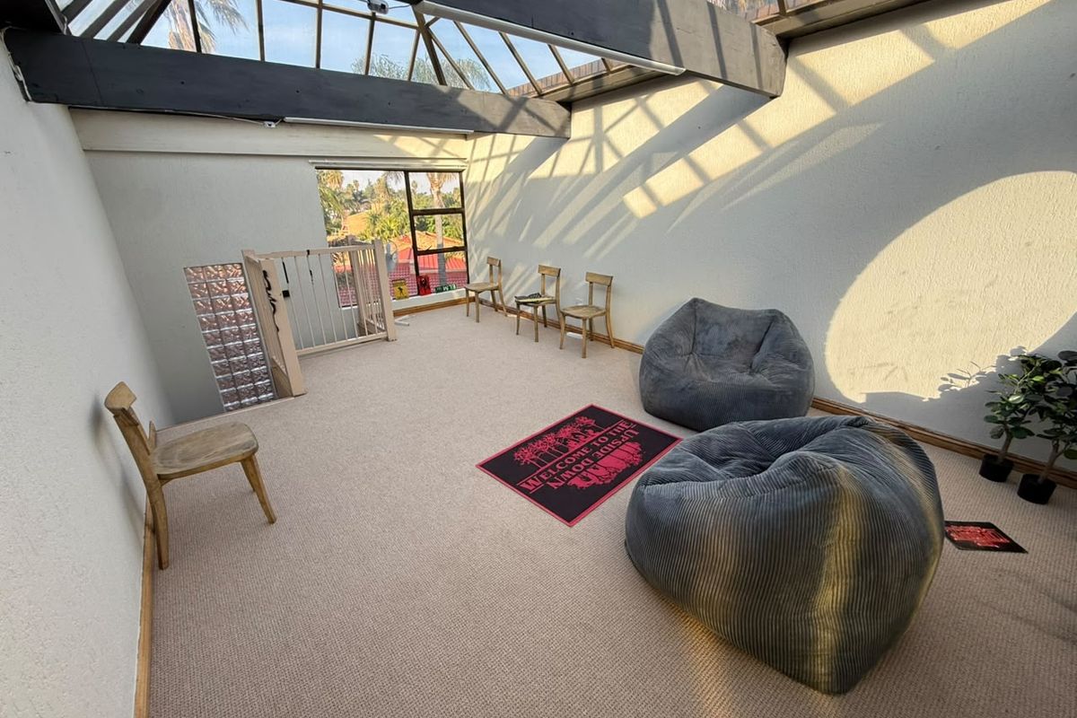 Spacious living area featuring a large skylight with exposed timber beams, carpeted flooring, and a unique glass block feature wall.