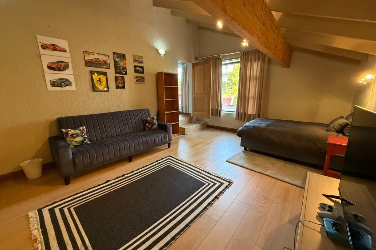 Spacious bedroom featuring exposed timber ceiling beams, laminate flooring, and direct access to an outdoor area.