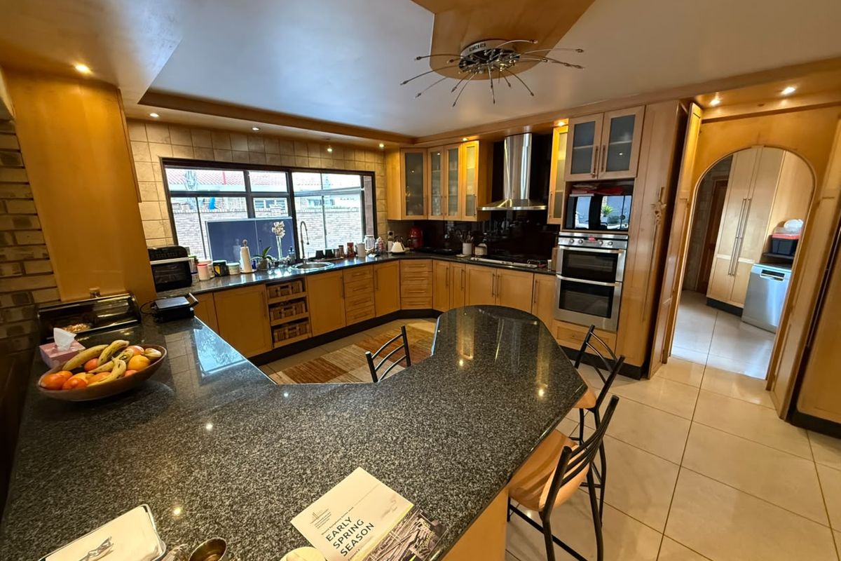Spacious kitchen featuring granite countertops, built-in oven, extractor fan, and ample cabinetry, with an open-plan layout and tiled flooring.