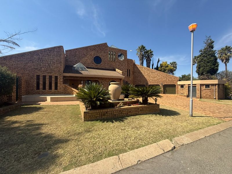 A distinctive face-brick residence featuring a paved driveway, triple garage, and unique architectural elements including skylights and a circular window.