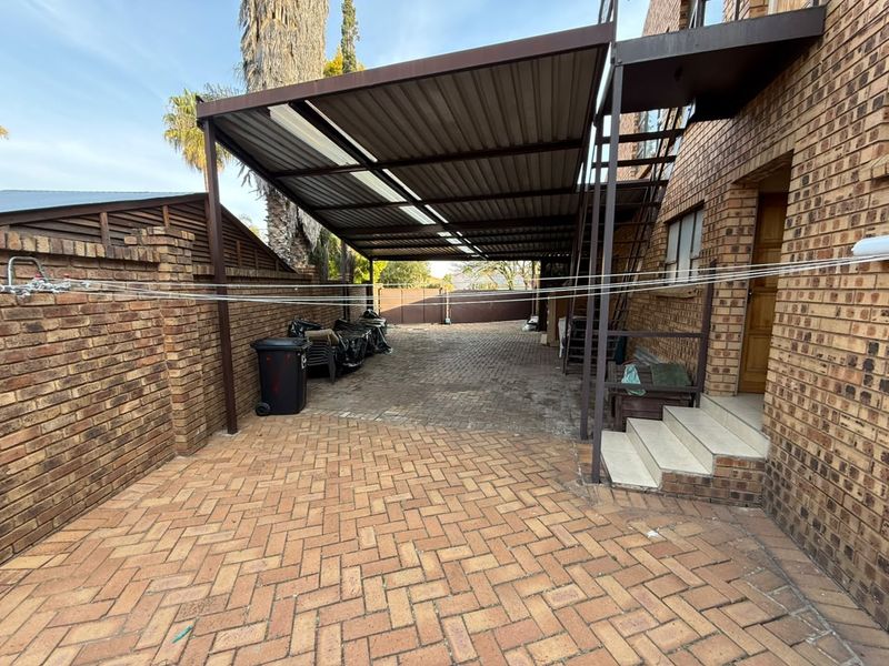 Rear exterior area featuring brick paving, a covered carport structure, and an external metal staircase leading to the upper level.