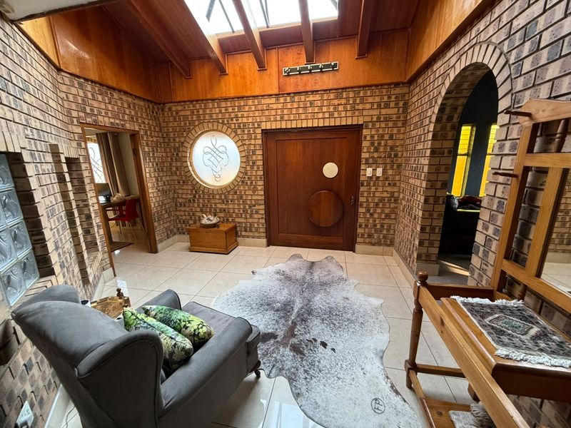 Spacious entrance hall featuring exposed brick walls, a timber vaulted ceiling with a skylight, and unique architectural details including a circular window and arched doorway.