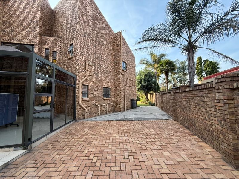 Rear exterior view of the property featuring a face brick facade, paved driveway, and an enclosed glass patio area.
