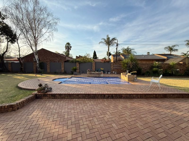 A well-maintained outdoor pool area featuring a brick-paved patio, a swimming pool with a cover, and secure brick boundary walls.