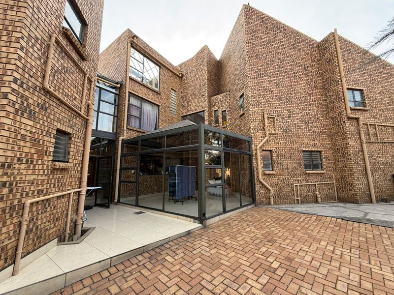 A rear exterior view of a multi-story face brick house featuring a modern glass-enclosed conservatory and a paved courtyard area.