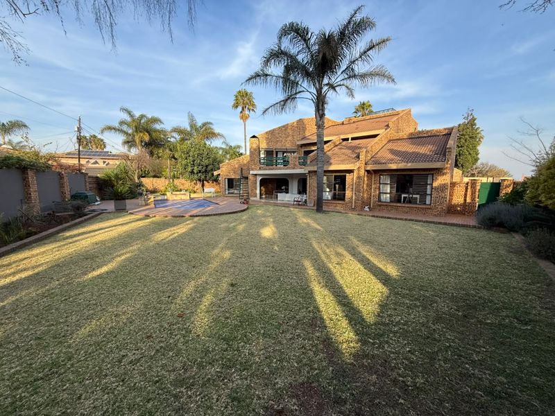 Spacious rear garden featuring a swimming pool, covered patio, and balcony, set against a multi-level brick house with a tiled roof.