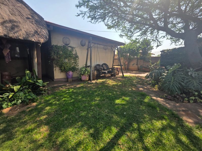 A rear garden area featuring a lawn, paved pathway, and a section of the house with a traditional thatched roof.