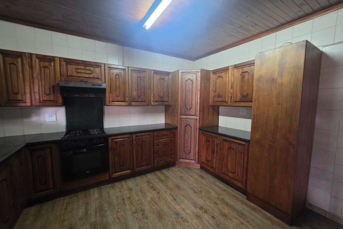 A functional kitchen featuring traditional wooden cabinetry, black countertops, built-in oven and hob, and a timber-paneled ceiling.