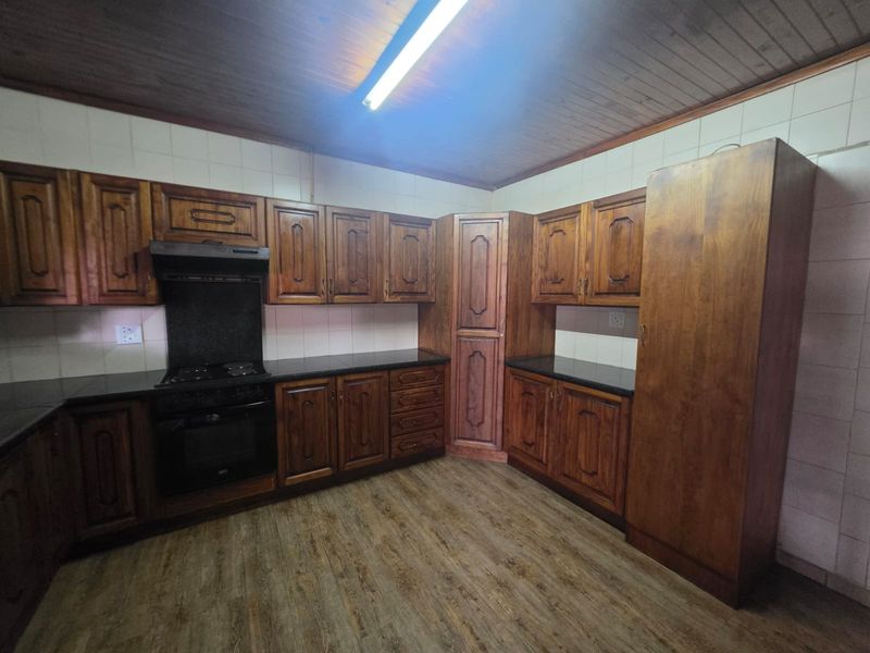 A functional kitchen featuring traditional wooden cabinetry, black countertops, built-in oven and hob, and a timber-paneled ceiling.