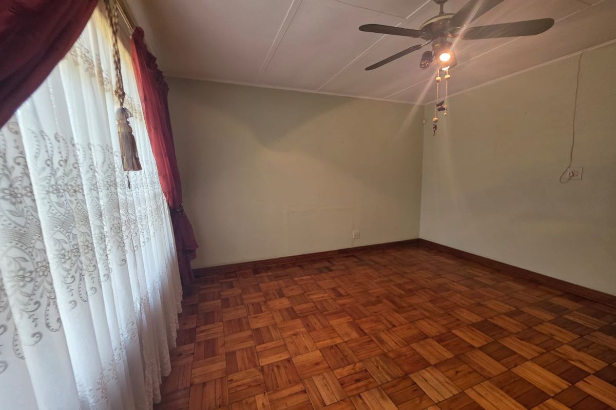 A vacant bedroom featuring classic parquet wood flooring, a ceiling fan, and neutral wall finishes, offering a clean canvas for personalization.