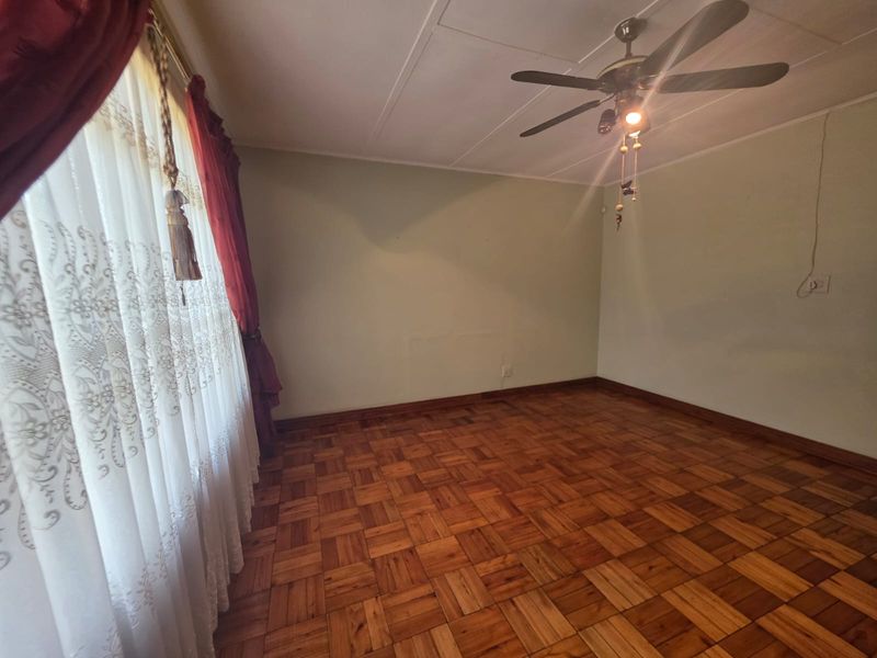 A vacant bedroom featuring classic parquet wood flooring, a ceiling fan, and neutral wall finishes, offering a clean canvas for personalization.