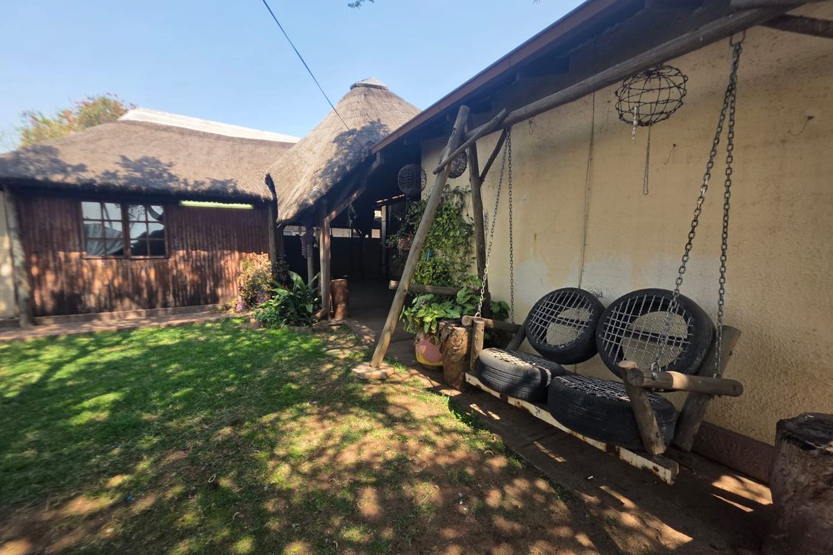 Rear garden area featuring a thatched roof structure, timber cladding, and a covered patio space with a rustic swing.
