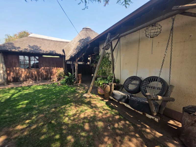 Rear garden area featuring a thatched roof structure, timber cladding, and a covered patio space with a rustic swing.
