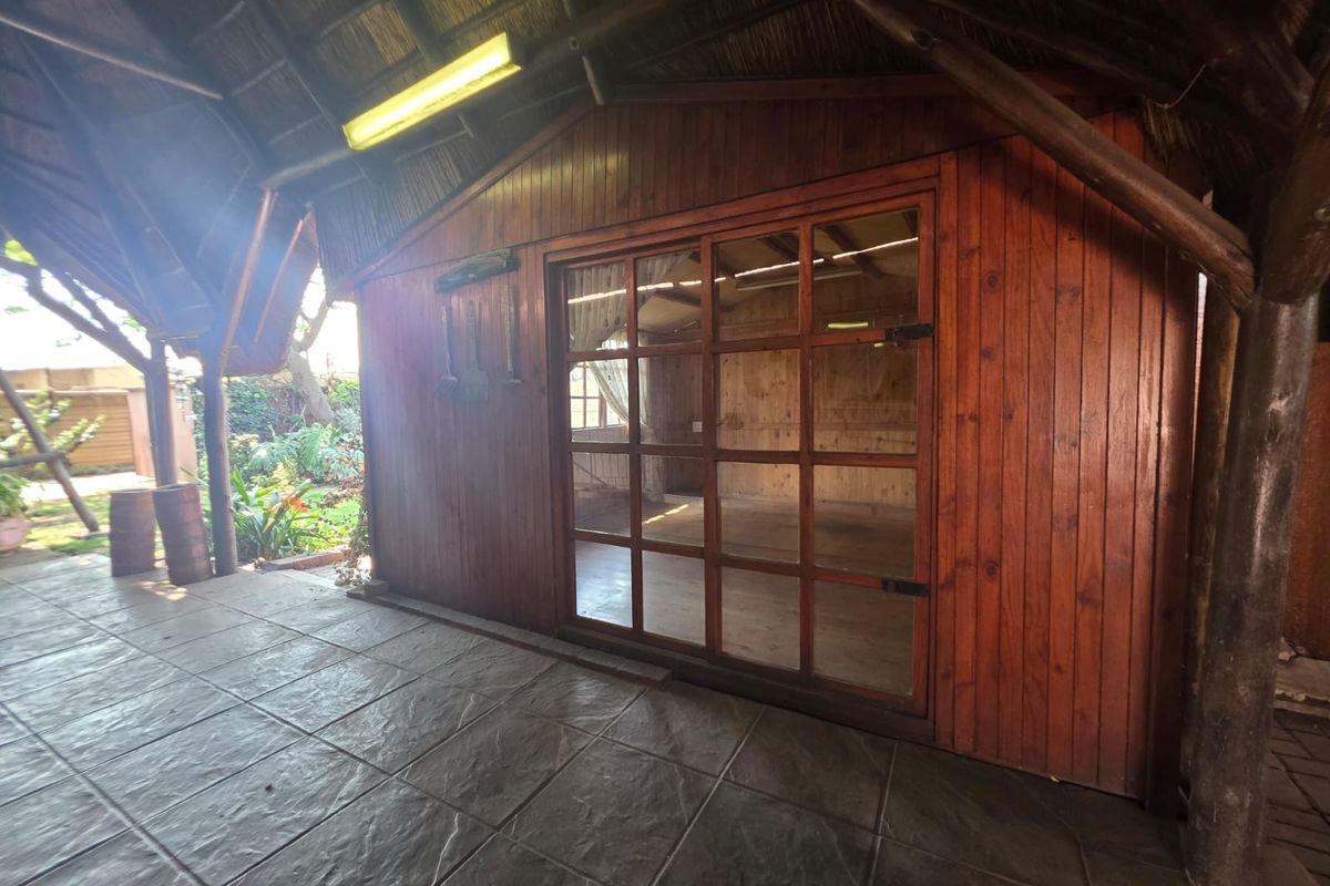 Covered outdoor patio area featuring a thatch roof, tiled flooring, and timber-clad walls with a large glass door leading to an interior space.