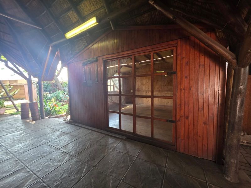 Covered outdoor patio area featuring a thatch roof, tiled flooring, and timber-clad walls with a large glass door leading to an interior space.