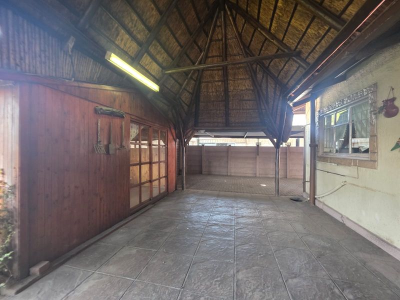 A covered outdoor patio area featuring a traditional thatched roof, tiled flooring, and timber wall cladding, providing a versatile space for outdoor living.