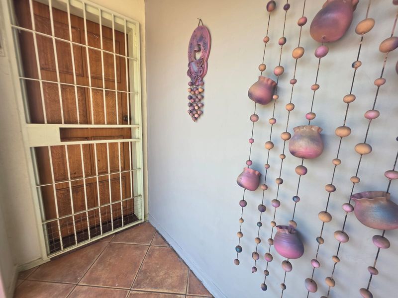 A covered entrance area featuring a wooden door with a security gate and tiled flooring.