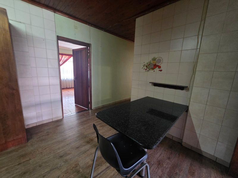 A dated kitchen area featuring tiled walls, a wooden ceiling, and a built-in stone breakfast bar, offering potential for modernization.