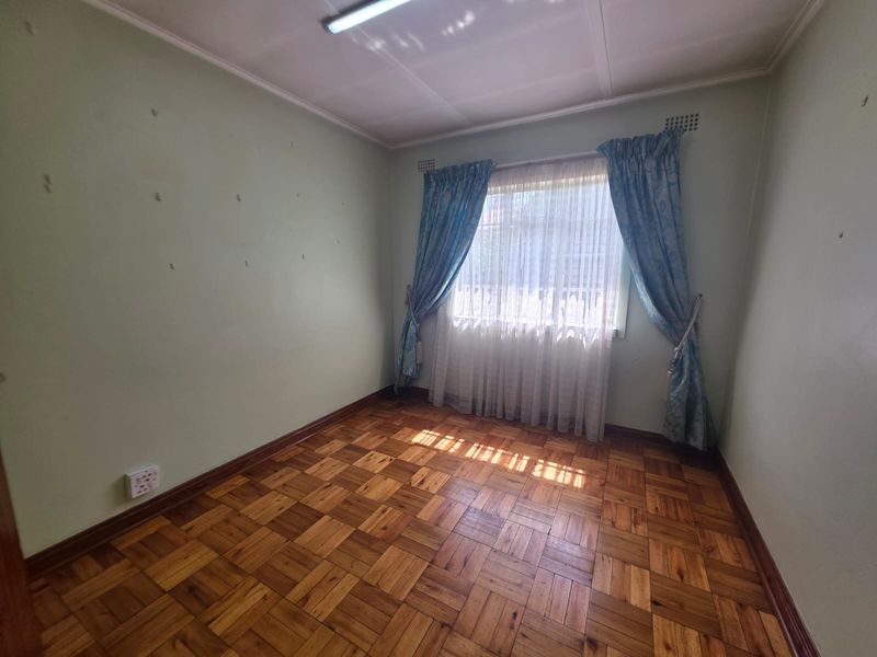 An empty bedroom featuring original parquet flooring, light green walls with surface imperfections, and a window with existing curtain tracks.