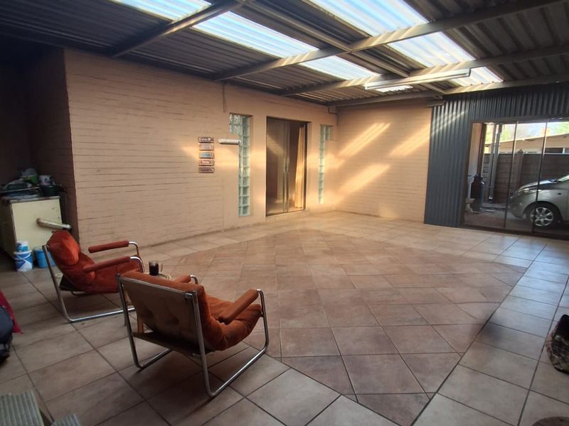 A spacious covered patio featuring tiled flooring, a corrugated roof with translucent panels, and glass sliding door access to the main house.
