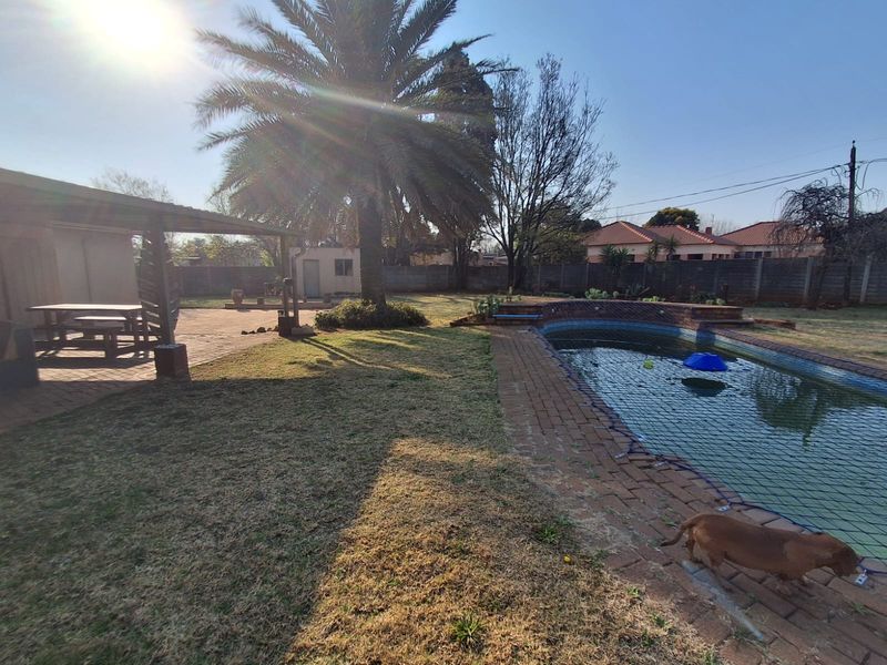 Spacious backyard featuring a swimming pool with safety net, brick-paved surround, and a covered patio area, set within a walled garden.